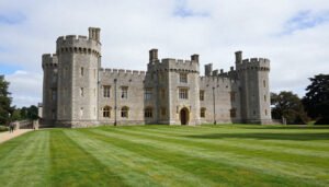 Château de Kerdurand en pierre, avec ses tours crénelées et sa vaste pelouse rayée, sous un ciel partiellement nuageux.