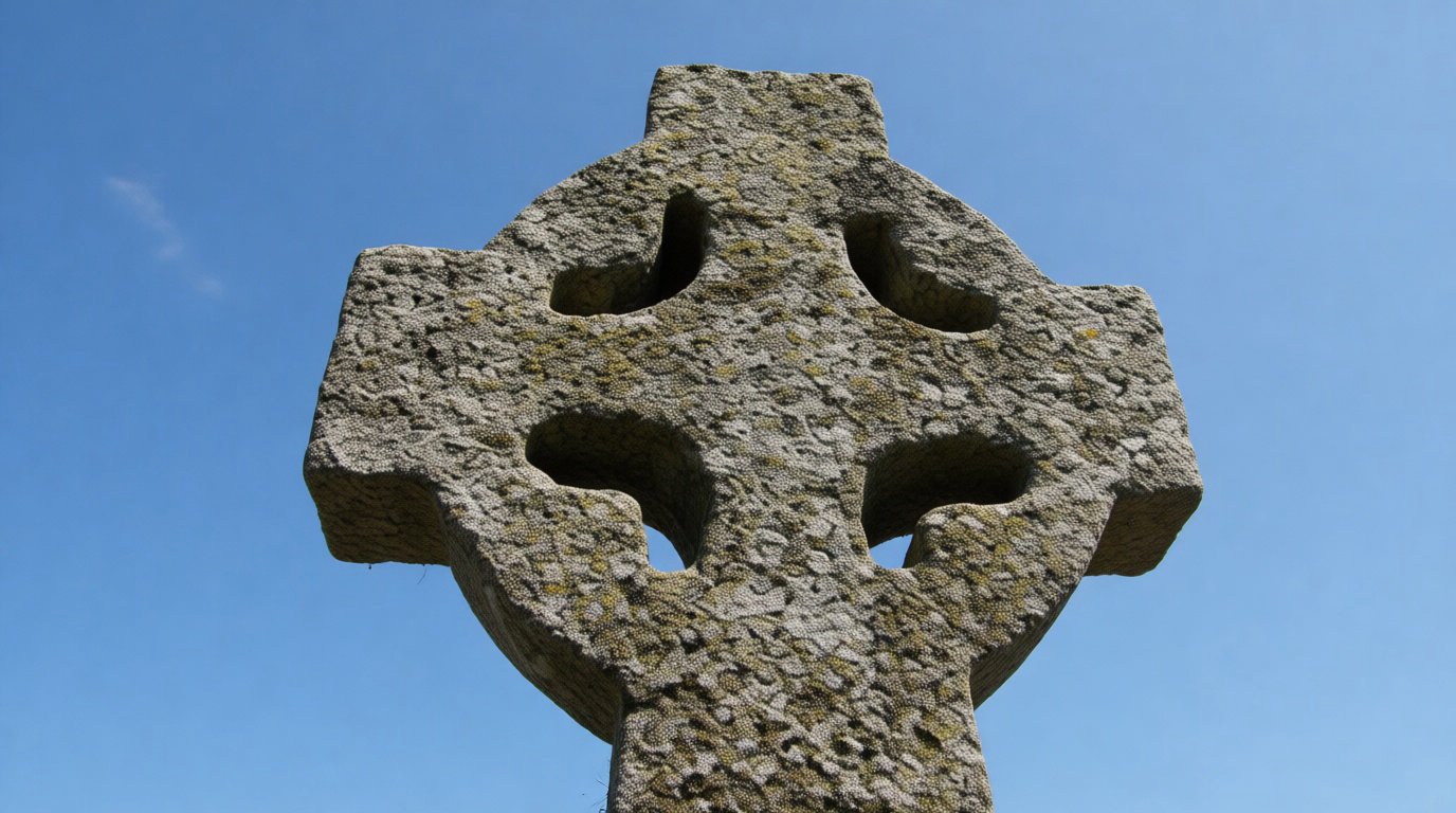 Une croix celtique en pierre, recouverte de mousse et de lichen, se dresse contre un ciel bleu clair. Des ouvertures circulaires marquent ses bras.